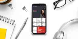 Image of the Swinburne app loaded onto a mobile phone with typical desk items around it (headphones, glasses, pen, notepad, bulldog clips).