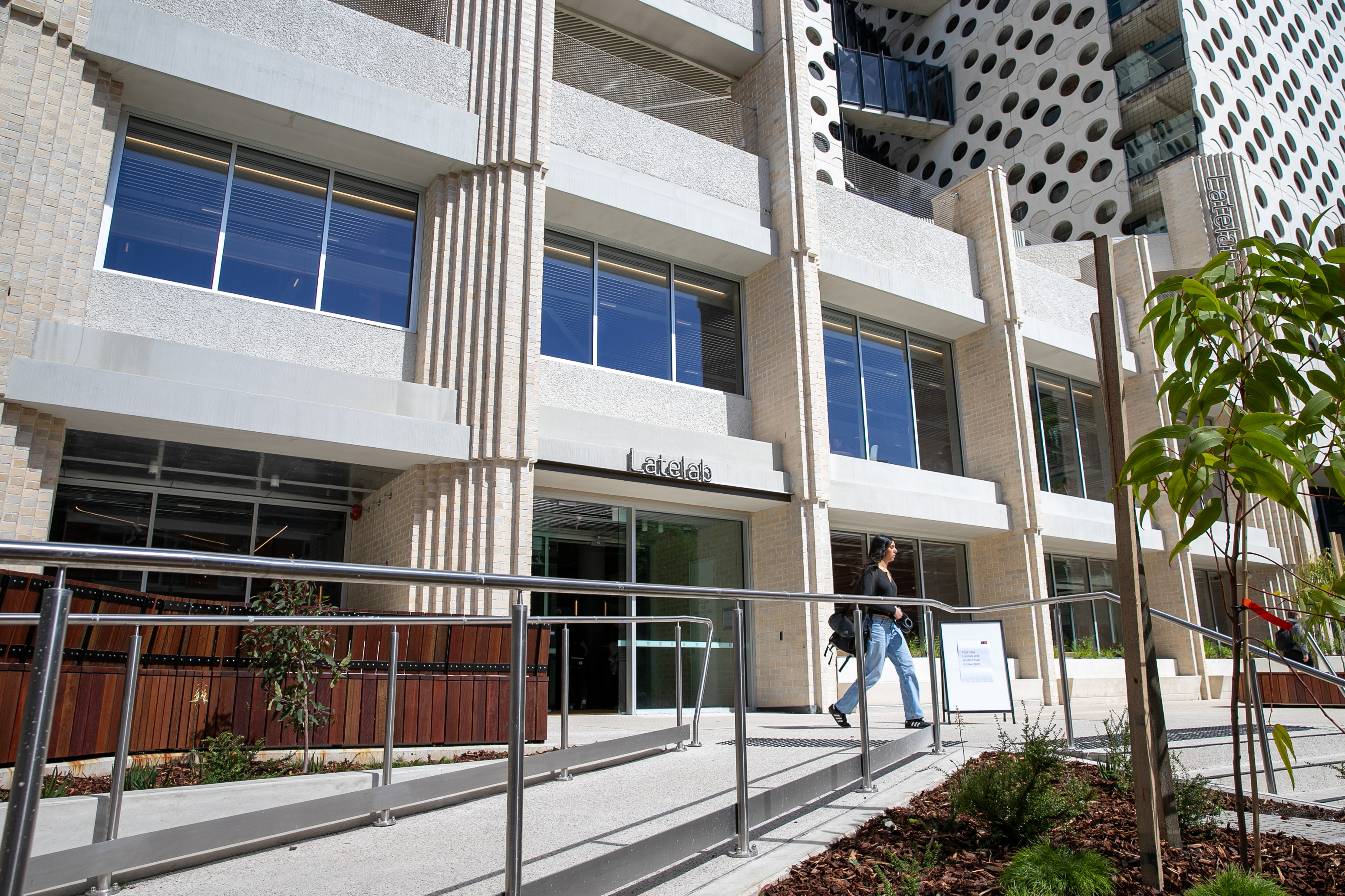 A young women walking with her shoulder study bag past a new study building
