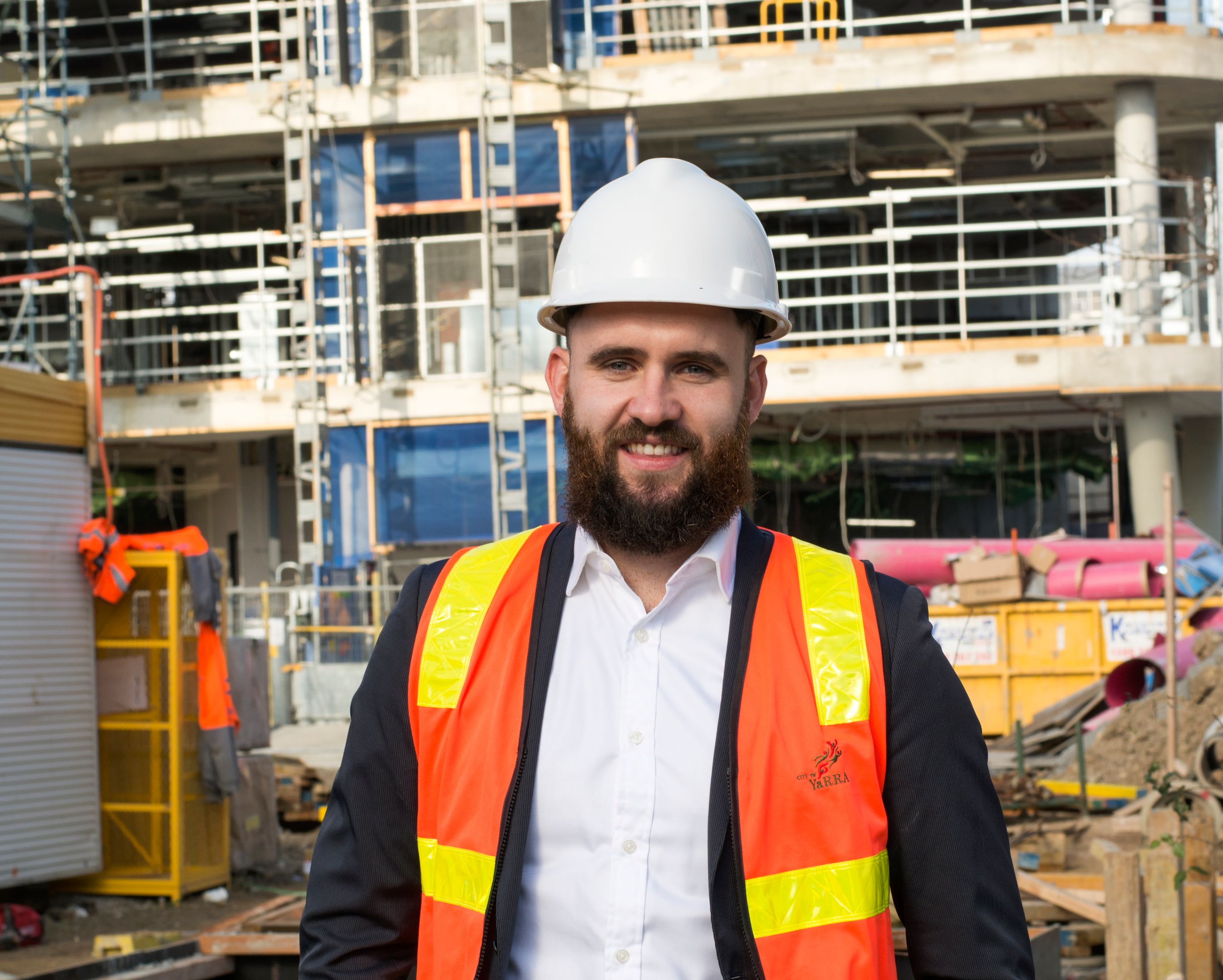 Peter Moran City of Yarra Photograph of Peter Moran standing in front of a construction site wearing a safety vest and hard hat.