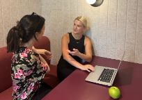 Two female working around a laptop and interacting with each other. 