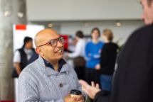 Man holding a coffee cup while conversing at the Swinburne 2026 Study Expo event with others in the background.