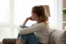 Upset woman sitting on couch alone at home looking out window