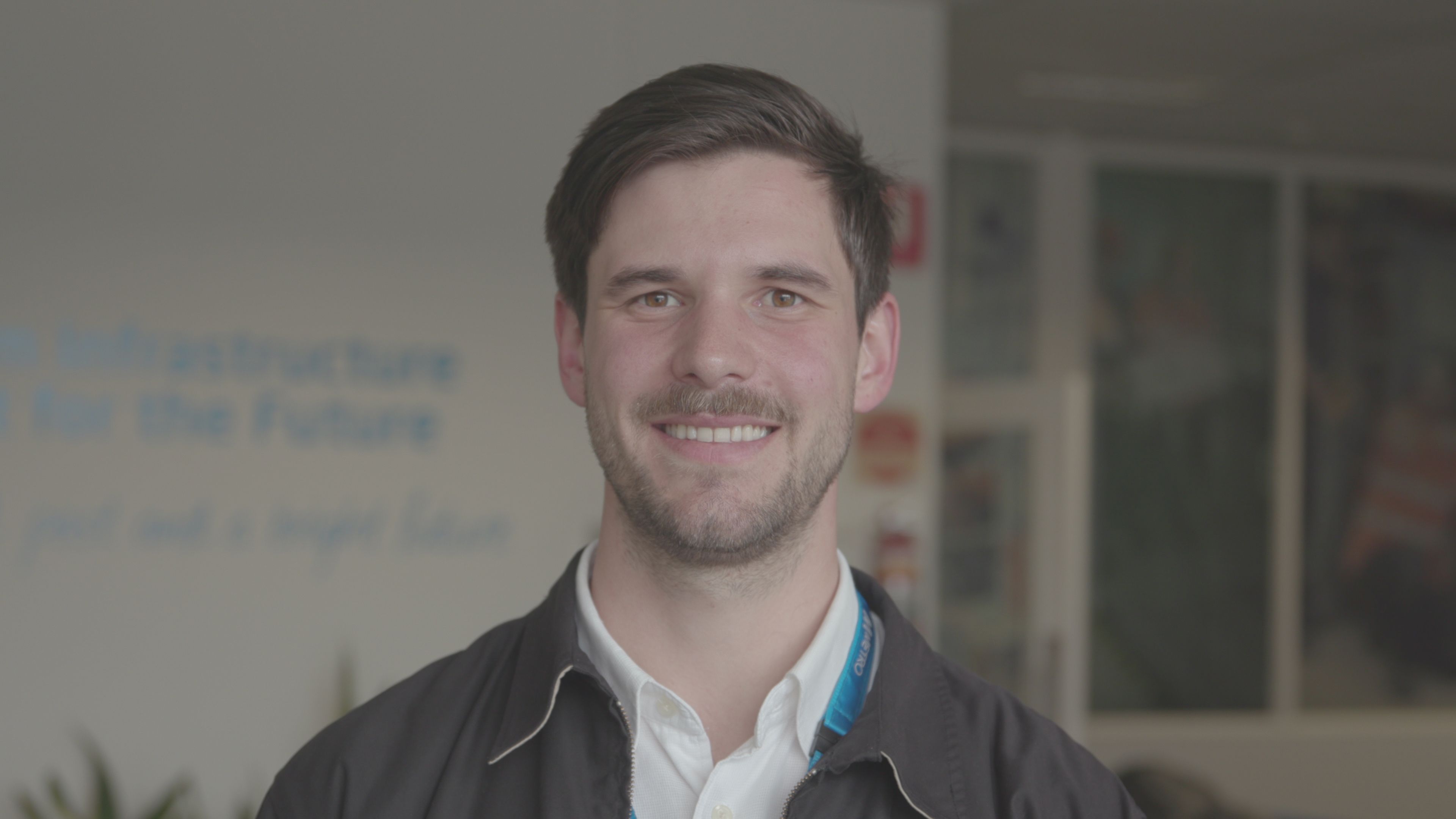 Nathan Loriente Metro Trains Photograph of Nathan Loriente from Metro Trains. Nathan wears a white collared shirt and jacket and is standing in front of an office.