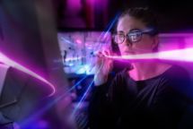 Woman staring at monitors in a dark office with neon light beaming through the image