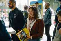 Female student attending open day wearing a red brown jacket waits to speak to staff