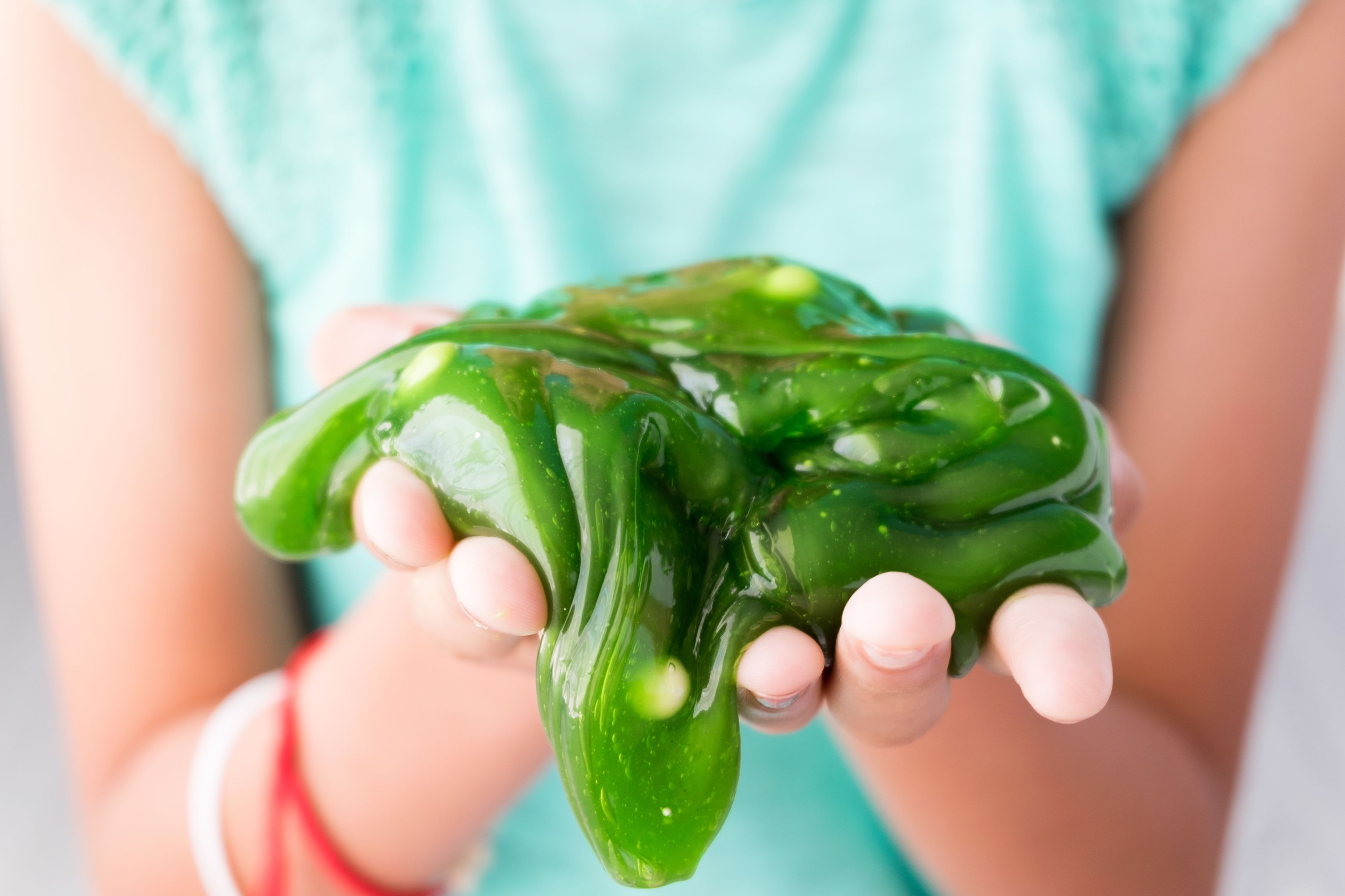 Children's hands cradling homemade green slime as part of a creative science experiment.