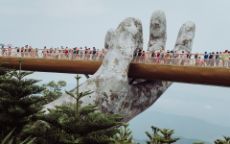 Pedestrian bridge in Vietnam held by large stone hands, with people walking across it.