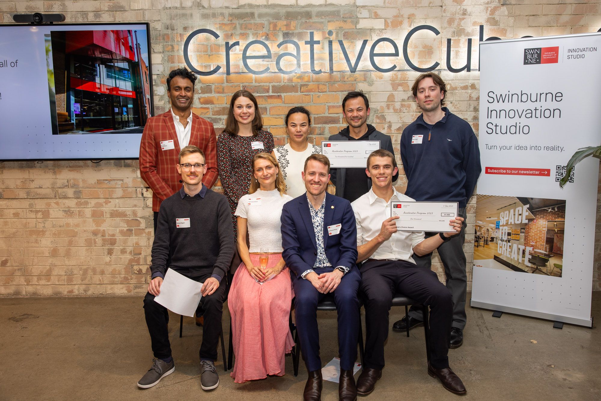 Swinburne Accelerator 2023 Demo Night Members of the Five startups at 2023 Swinburne Accelerator Program Demo Night. There a nine people in total, four sitting in from of five people standing. Everyone is smiling at the camera and a few are holding up award certificates