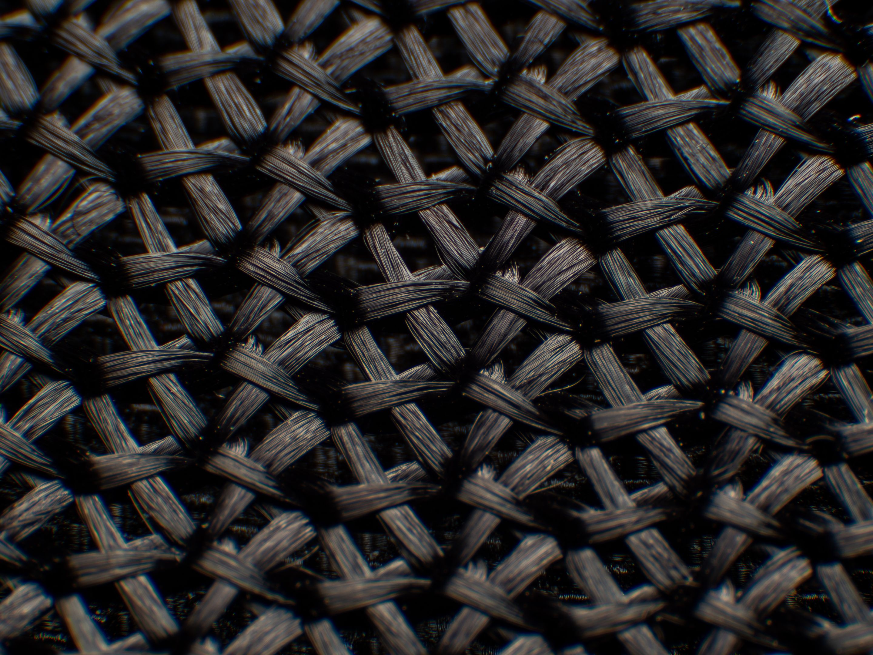 Close-up of synthetic fabric, black fiber. There is a large gap between the fibers, neatly woven, the fibers are glossy, high magnification, super macro. Synthetic fabric seen under magnification, showing the ordered, interlocked nature of the fabric.