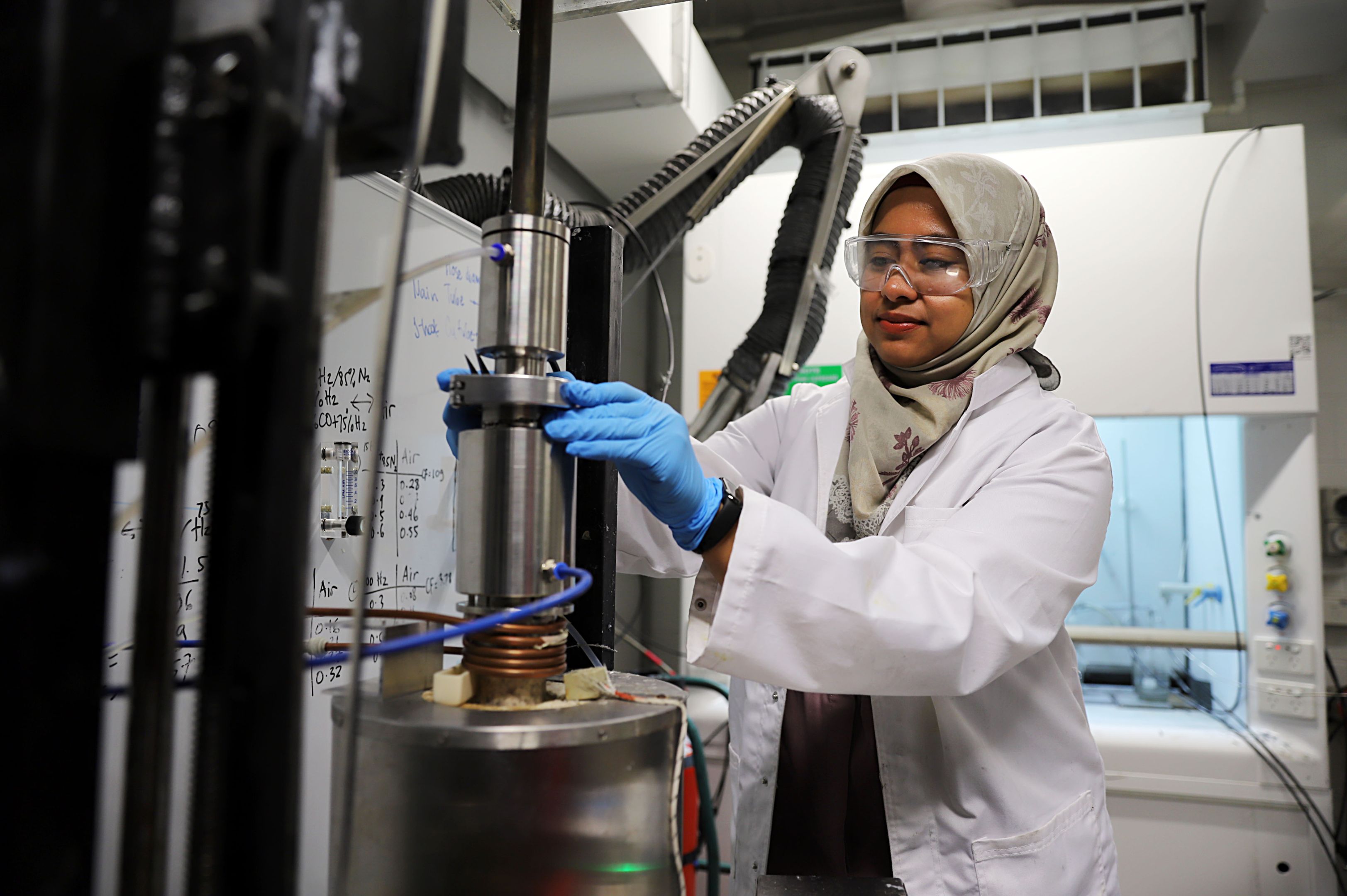Green steel revolution: How Swinburne researchers are tackling the global climate emergency in steel manufacturing A woman in a lab coat, protective eye glasses and latex gloves operates machinery in a scientific research lab