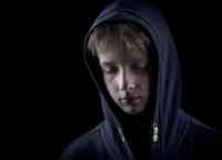 Headshot of sad child in the dark with a hood.