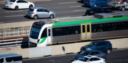 A freeway with cars driving and a train in the middle lane.