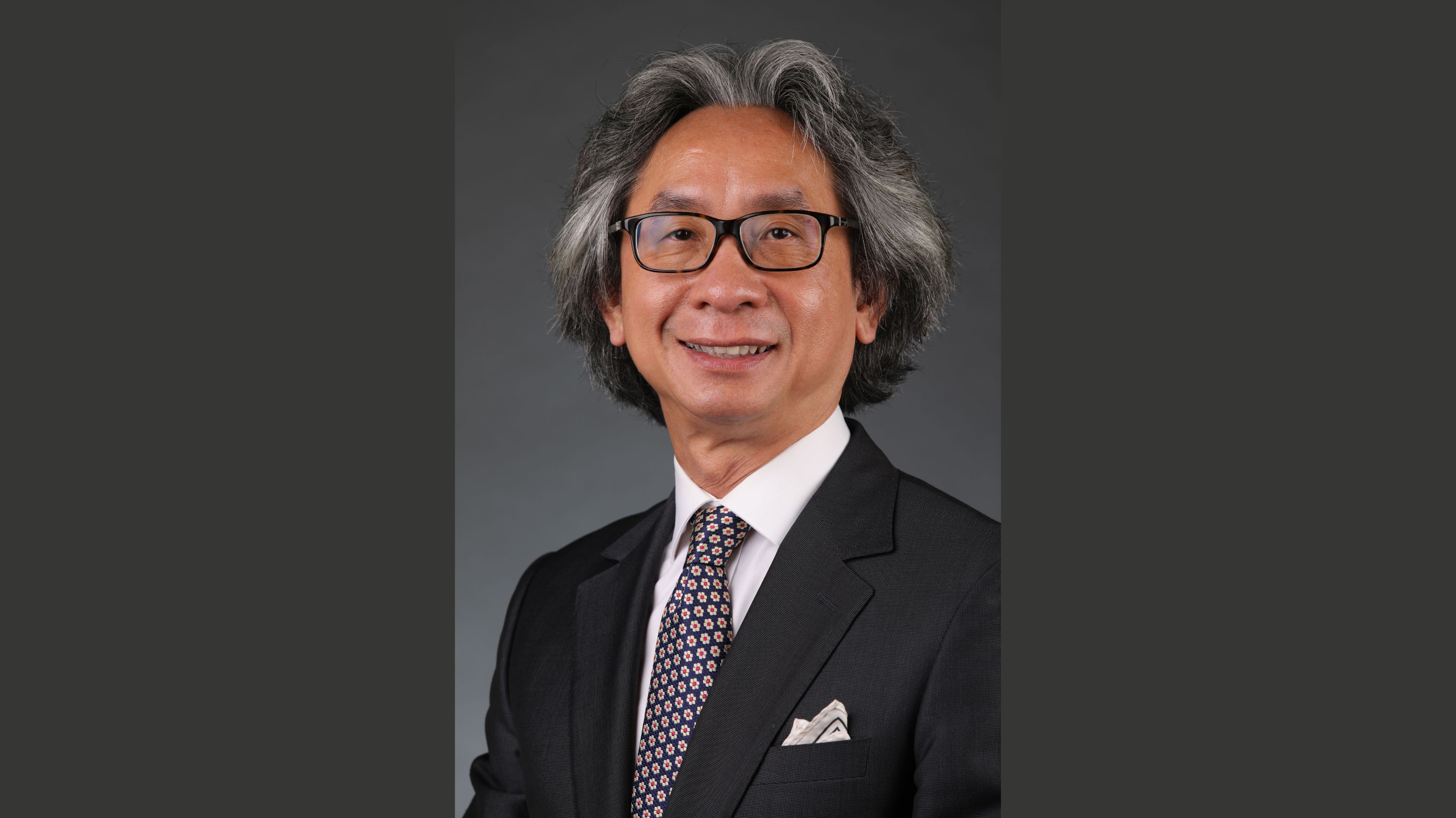 Man wearing glasses looking directly at the camera in front of a neutral background