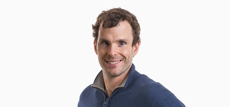 A man wearing a blue jacket is smiling at the camera