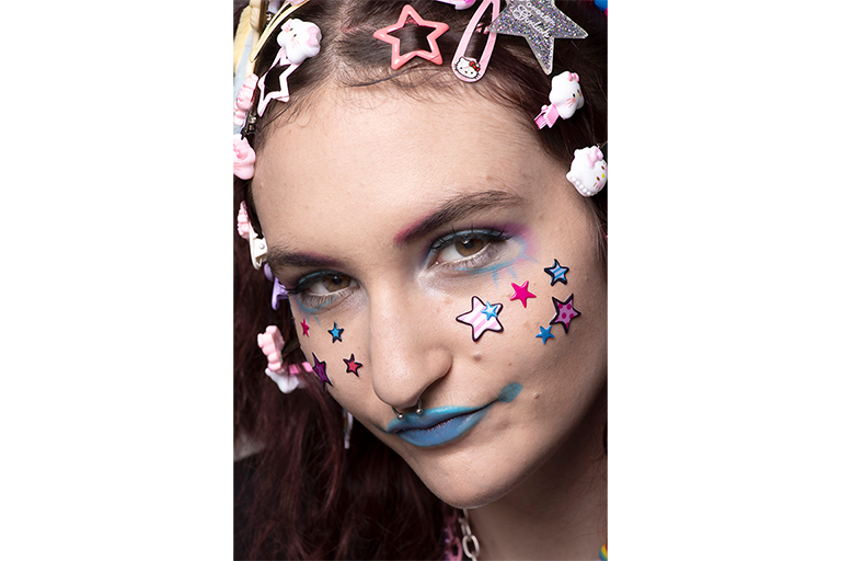 Close-up portrait of a person with colourful star stickers, bold makeup and playful hair clips.