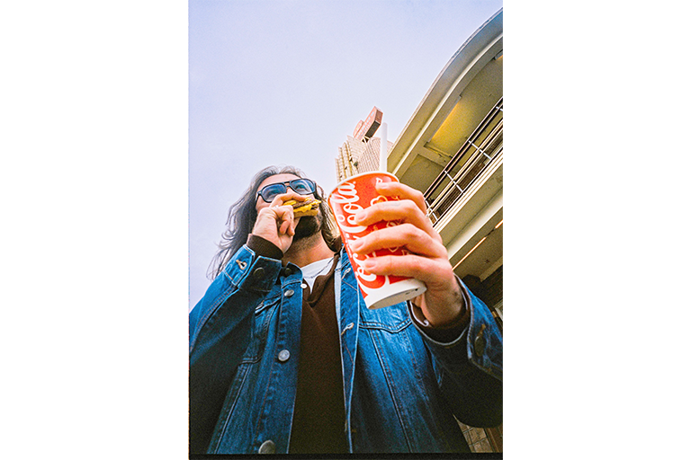 Low-angle photo of a person holding a drink cup and eating outdoors.