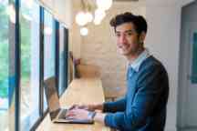 Portrait of a young adult male sat using his laptop in a modern office