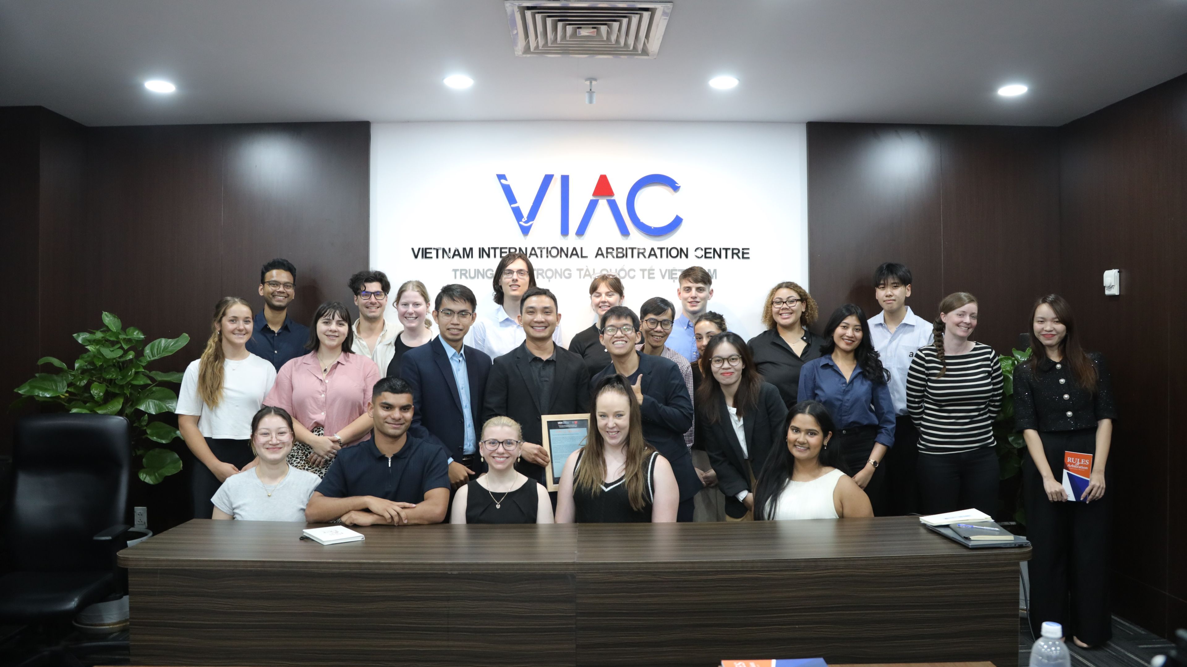 Vietnam Law, Governance and Culture Tour: Vietnam International Arbitration Centre A group of students and staff in a contemporary office with the Vietnam International Arbitration Centre logo on the wall behind them