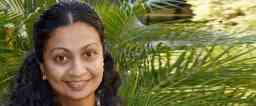 Female with light brown skin and dark brown hair smiling at the camera