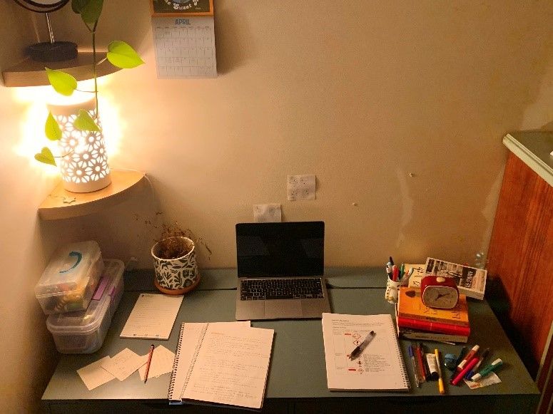 Ingrid has made a cozy study corner for herself in her bedroom. Ingrid’s desk, warmly lit and with scattered study materials, a pot plant and a stack of novels.