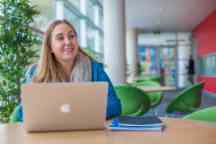 Student sitting at her desk working on her laptop with books beside her