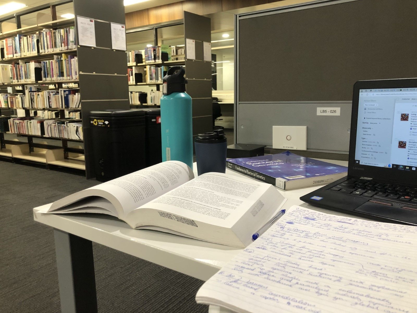Riddhi’s more likely to study out of home and in the library. A desk in the Swinburne library with a laptop, open textbooks and a water bottle.