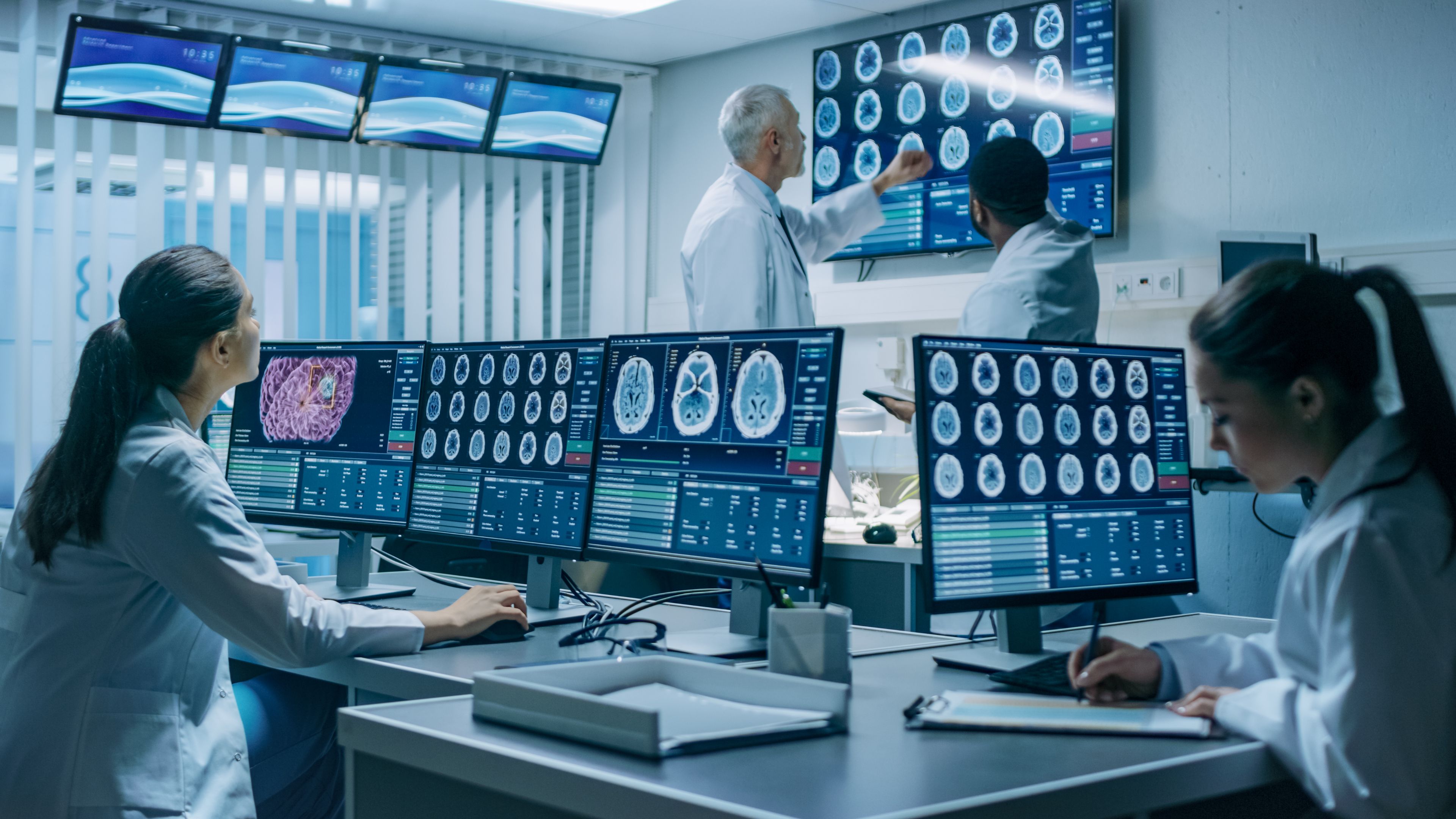 Neurologists at work in the brain research laboratory CT MRI scans Neurologists / neuroscientists surrounded by monitors showing CT, MRI scans having discussions.