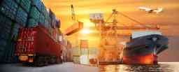 Cargo being loaded onto a ship during sunset. Airplane taking off in the background.