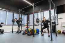 A male and female student wearing black Swinburne apparel using a squat rack