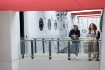 Two students standing and talking on internal walkway between two buildings.